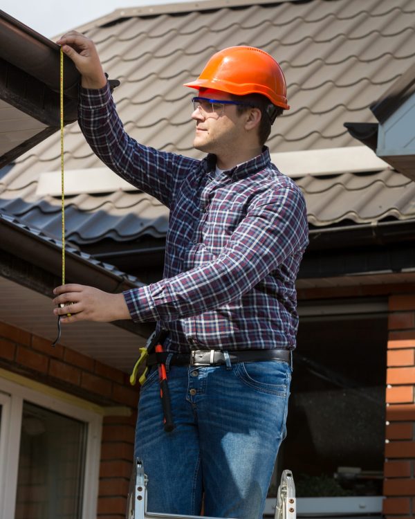 Portrait of professional worker measuring height of roof with tape
